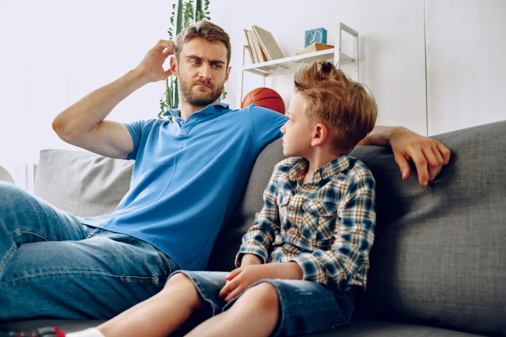Father and young son sitting together on a sofa in conversation at home