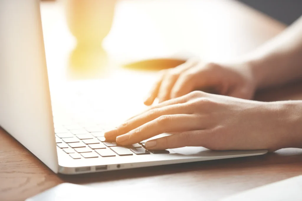 Close up of hands typing on a laptop keyboard in warm daylight