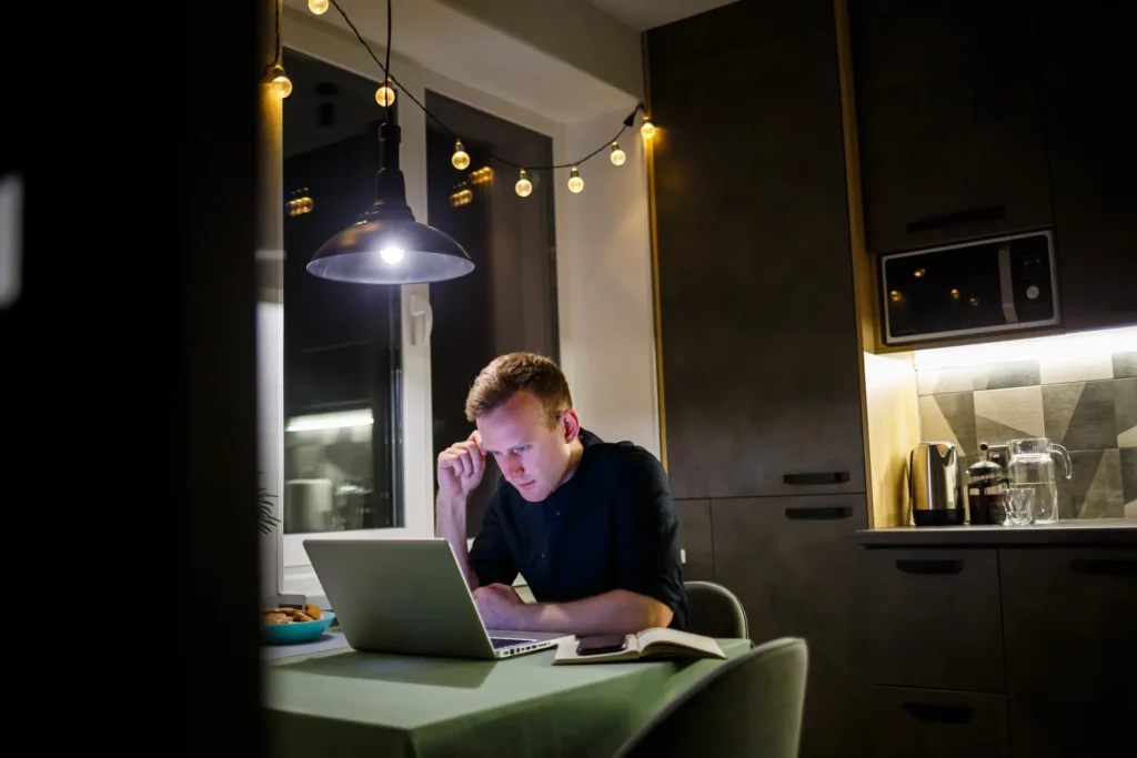 Man working alone on a laptop at a kitchen table in the evening