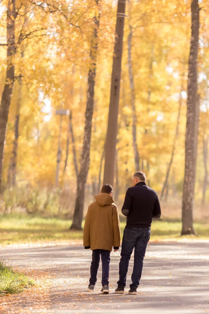 A parent and teenager walking together along a tree lined path in autumn