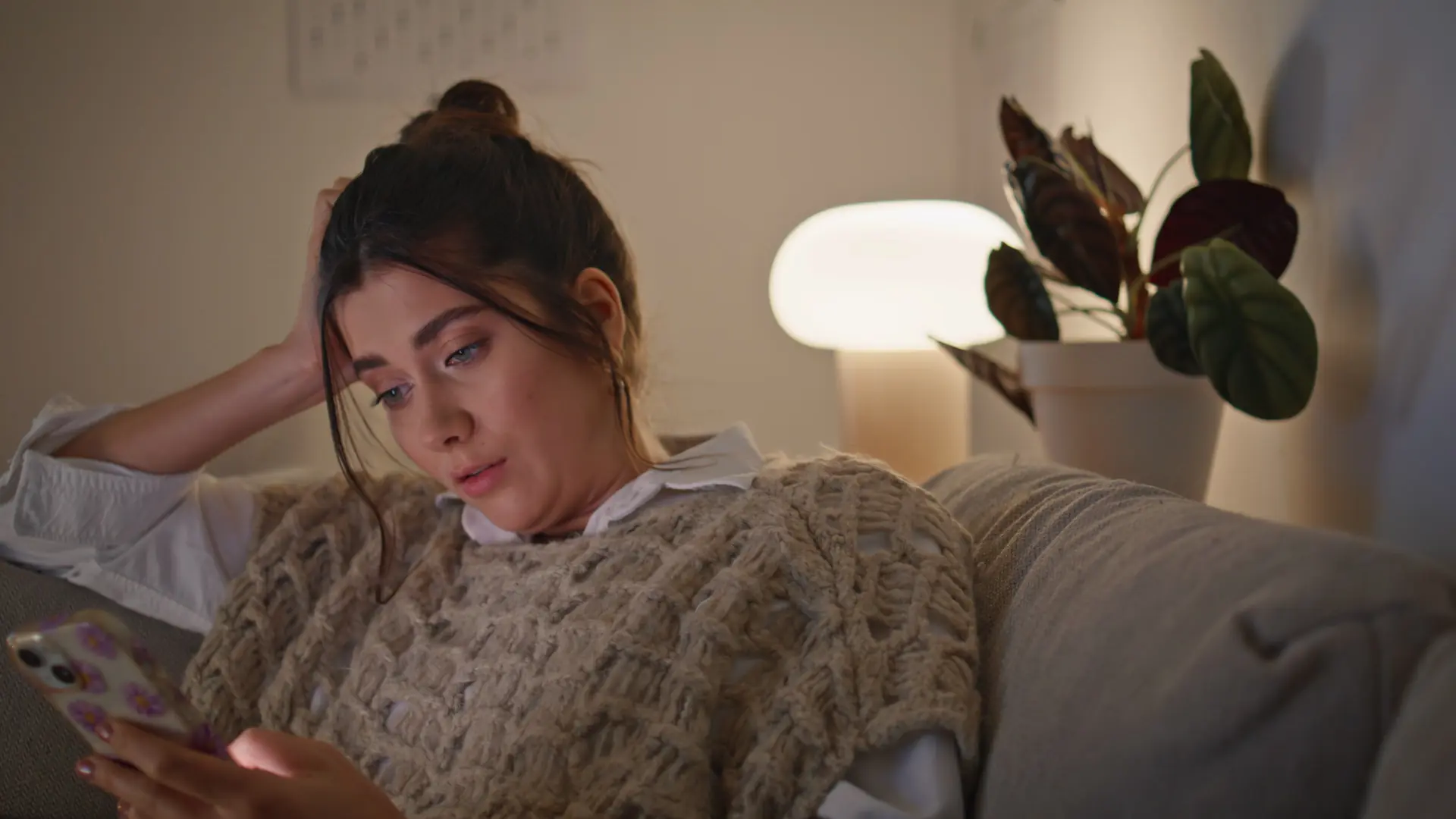 Woman sitting on a sofa at home looking thoughtfully at her phone Woman sitting on a sofa at home looking thoughtfully at her phone