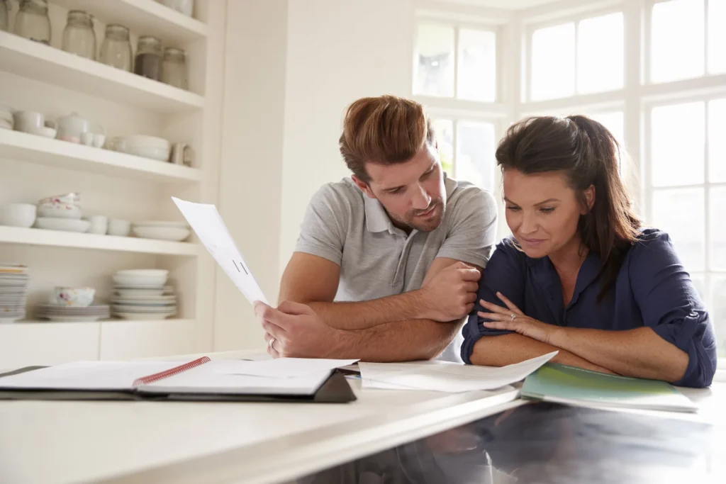 A couple standing at a kitchen counter, one holding a printed statement while the other reads it