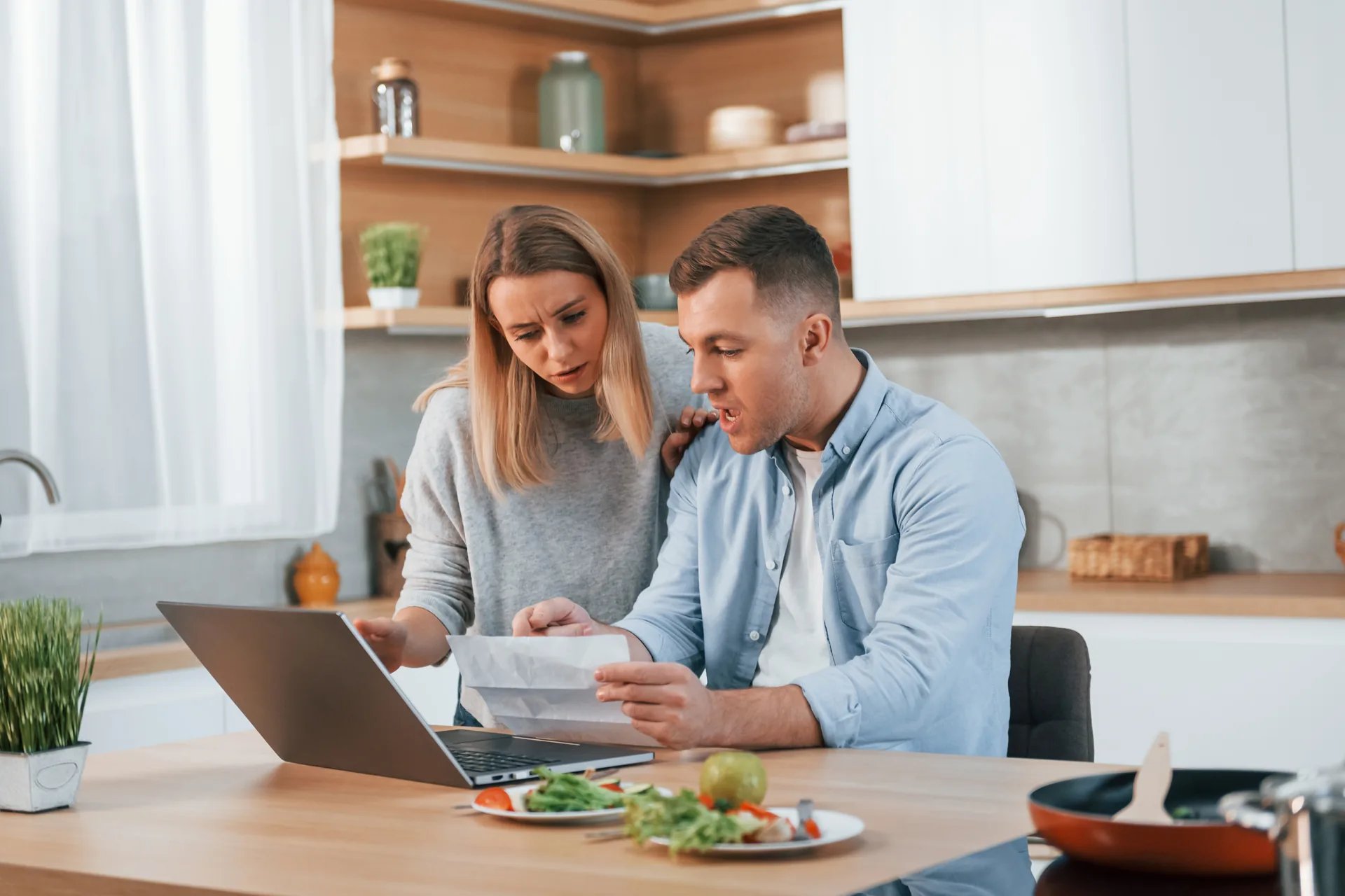Couple reviewing separation paperwork at a kitchen table A man and a woman sitting at a kitchen table looking carefully at a document beside an open laptop