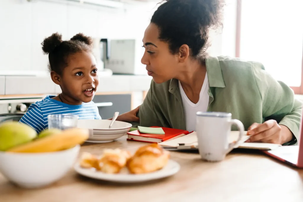 A mother and her young daughter talking over breakfast at a kitchen table