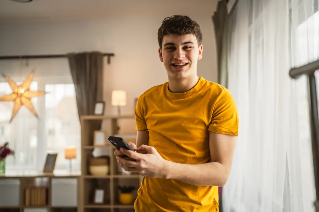 A teenage boy standing in a bright living room looking at his smartphone